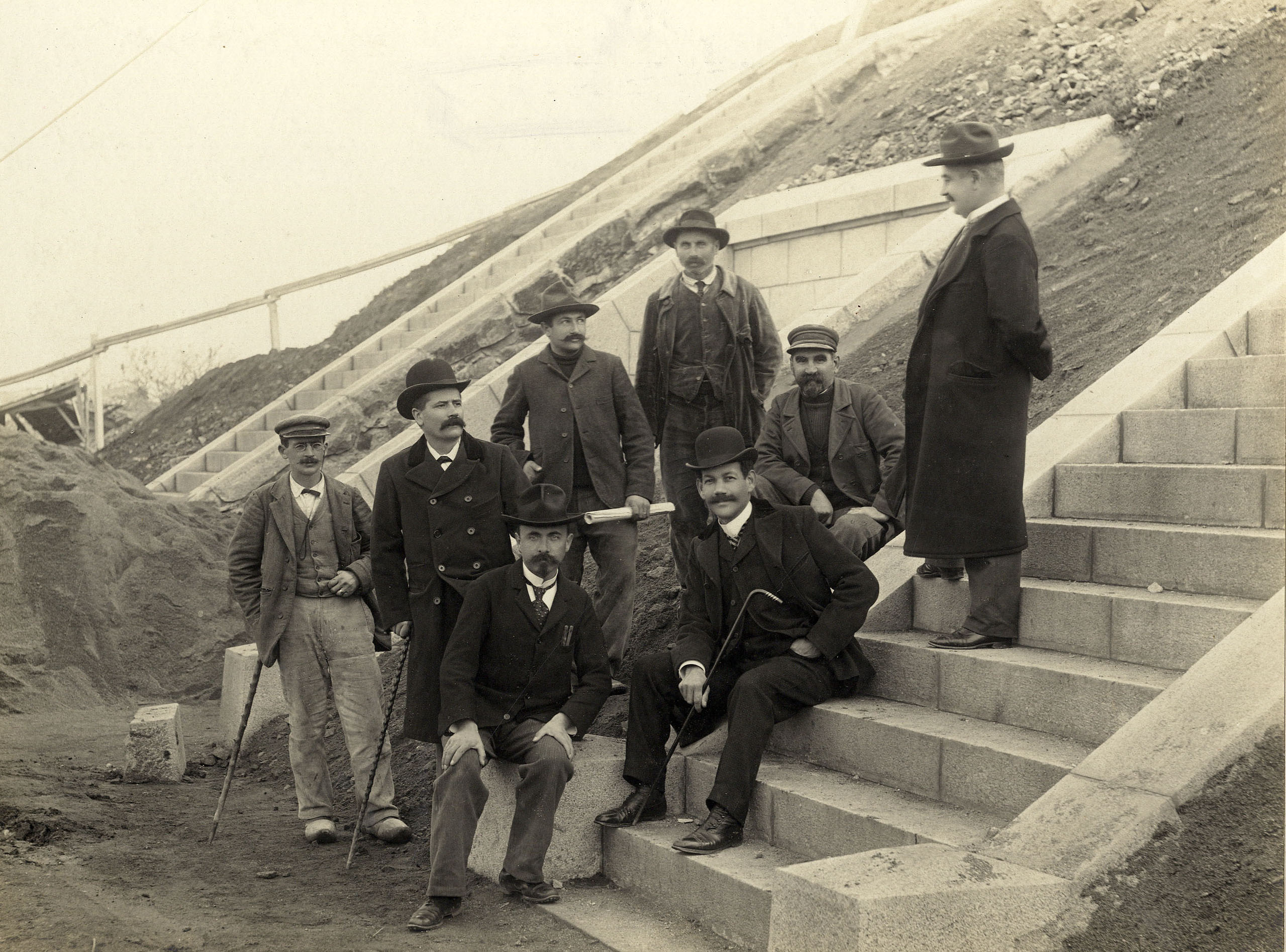 Huit hommes, dont Gaston Michel, l'ingénieur en chef de la Ville, et son adjoint Louis Primault, posent sur les marches en bas du réservoir lors d’une visite du chantier en 1904 (26Fi1078)