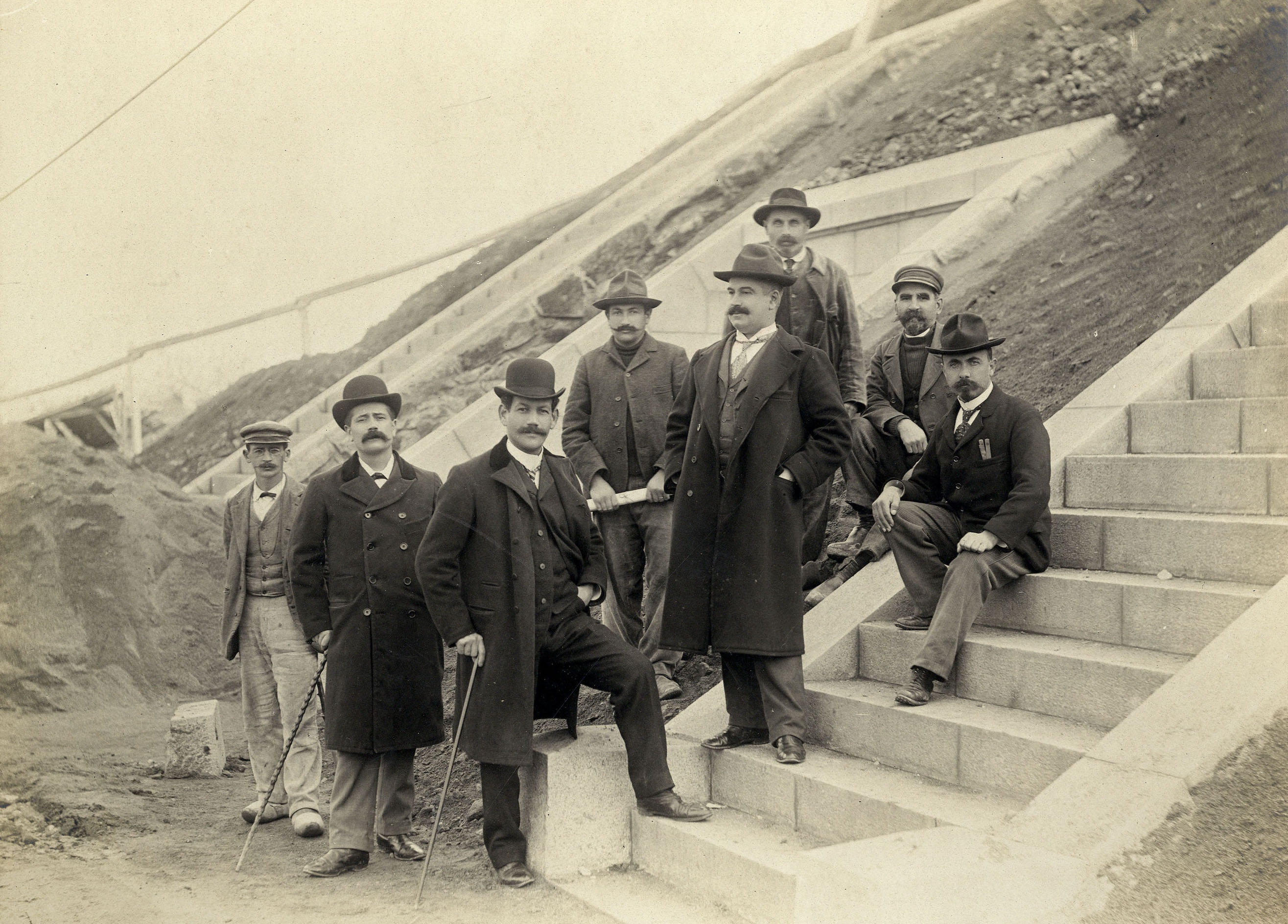 Huit hommes, dont Gaston Michel, l'ingénieur en chef de la Ville, et son adjoint Louis Primault, posent sur les marches en bas du réservoir lors d’une visite du chantier en 1904 (26Fi1079)