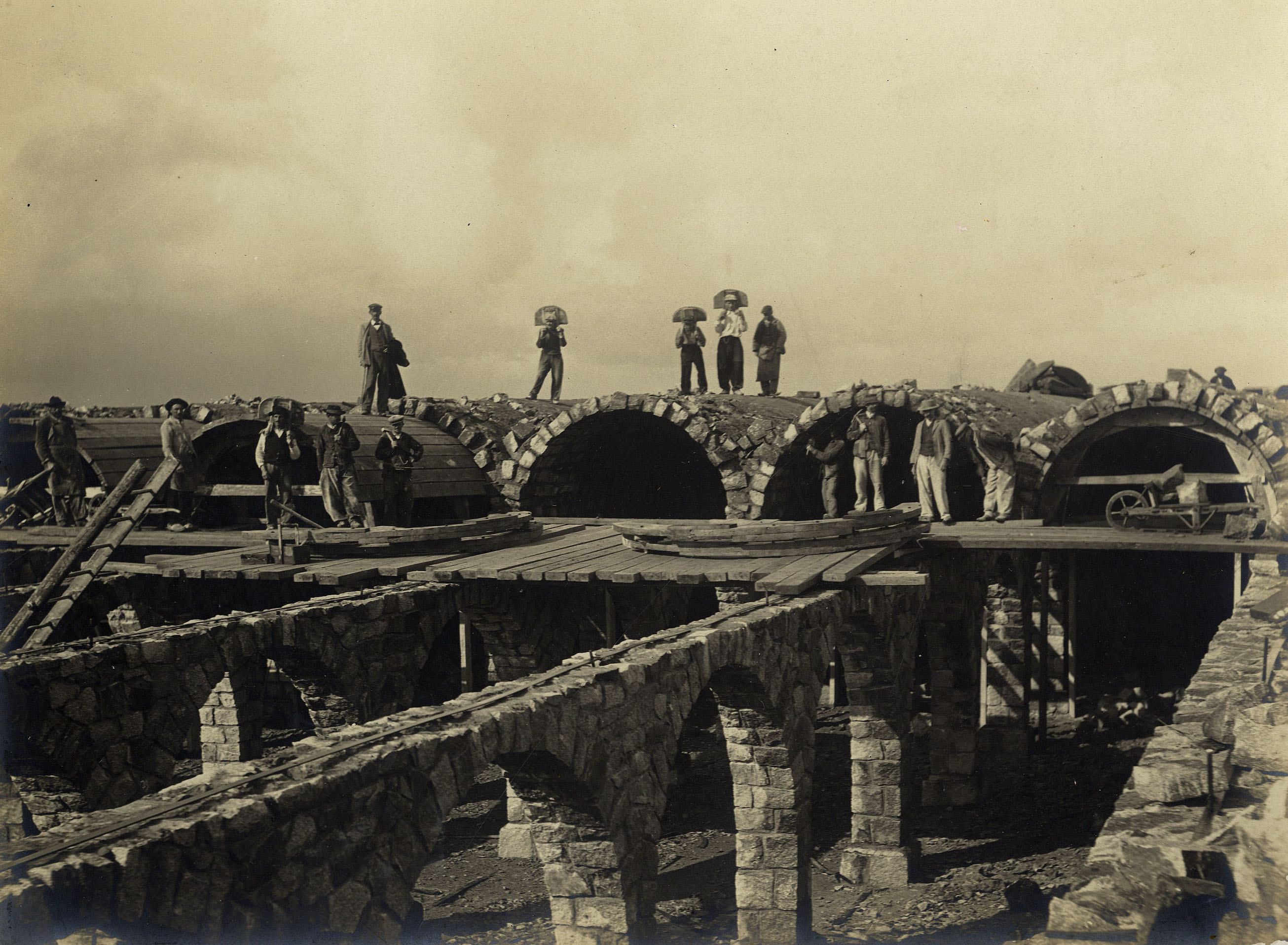 Des ouvriers et des porteurs de matériaux posent au sommet des voûtes du réservoir en 1902 (26Fi1085)