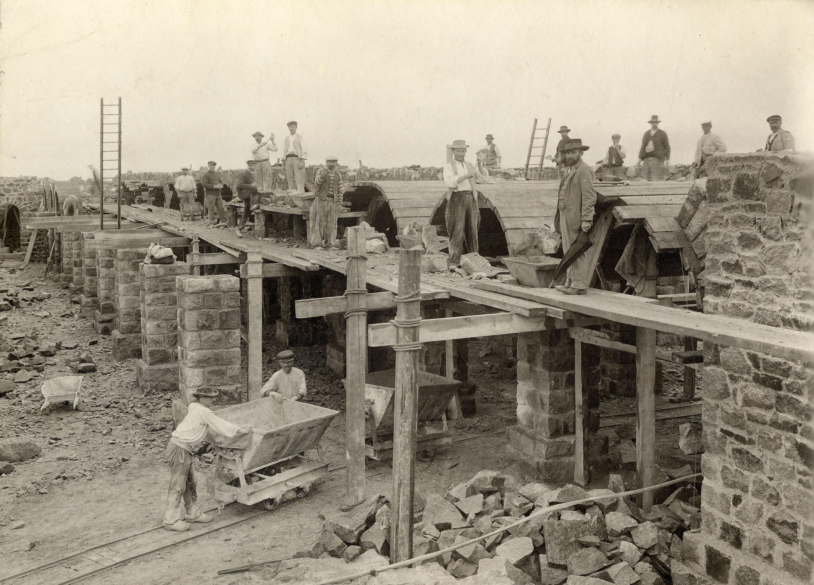 Des ouvriers sur le chantier du réservoir d’eau de la Contrie en 1903. Au premier plan, deux ouvriers poussent un wagonnet « Deauville » (26Fi1086)