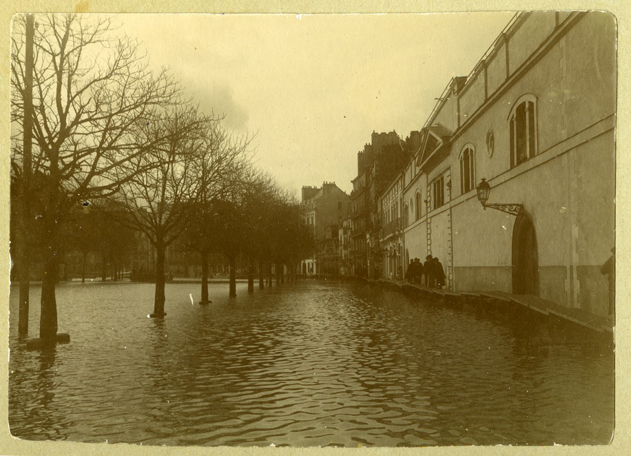 Vue de l'Erdre en crue, sur le quai des Tanneurs. Des piétons circulent sur des passerelles de bois rehaussées, le long du mur de l'usine à gaz. Dans le prolongement, vue de la quincaillerie Aubert et Thouvenin (123Z376)