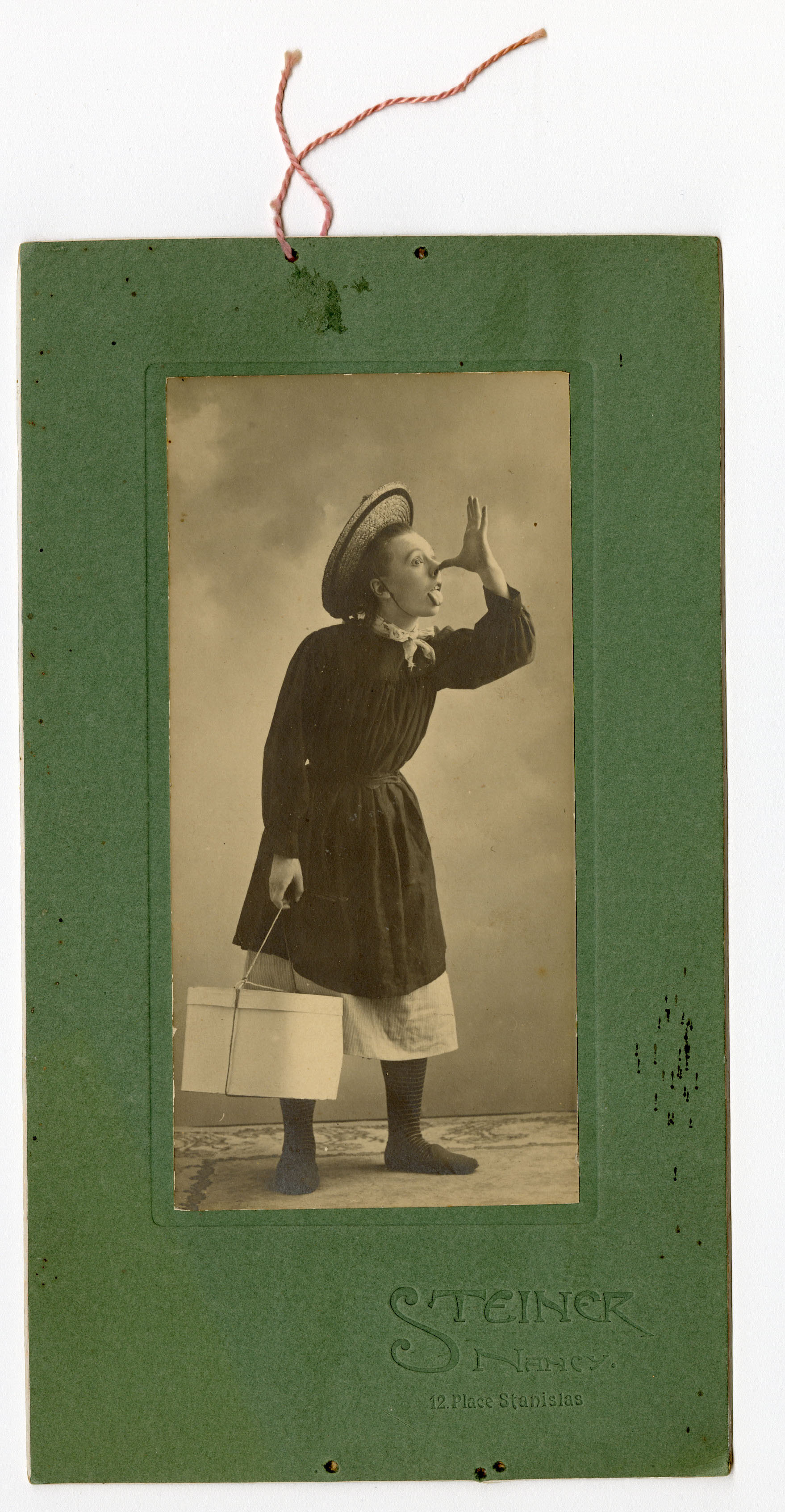 Photographie en noir et blanc par le photographe Steiner de Nancy de Francine Vasse grimaçant accoutrée d'un chapeau et tenant à la main une boîte, 1903 (199Z2)