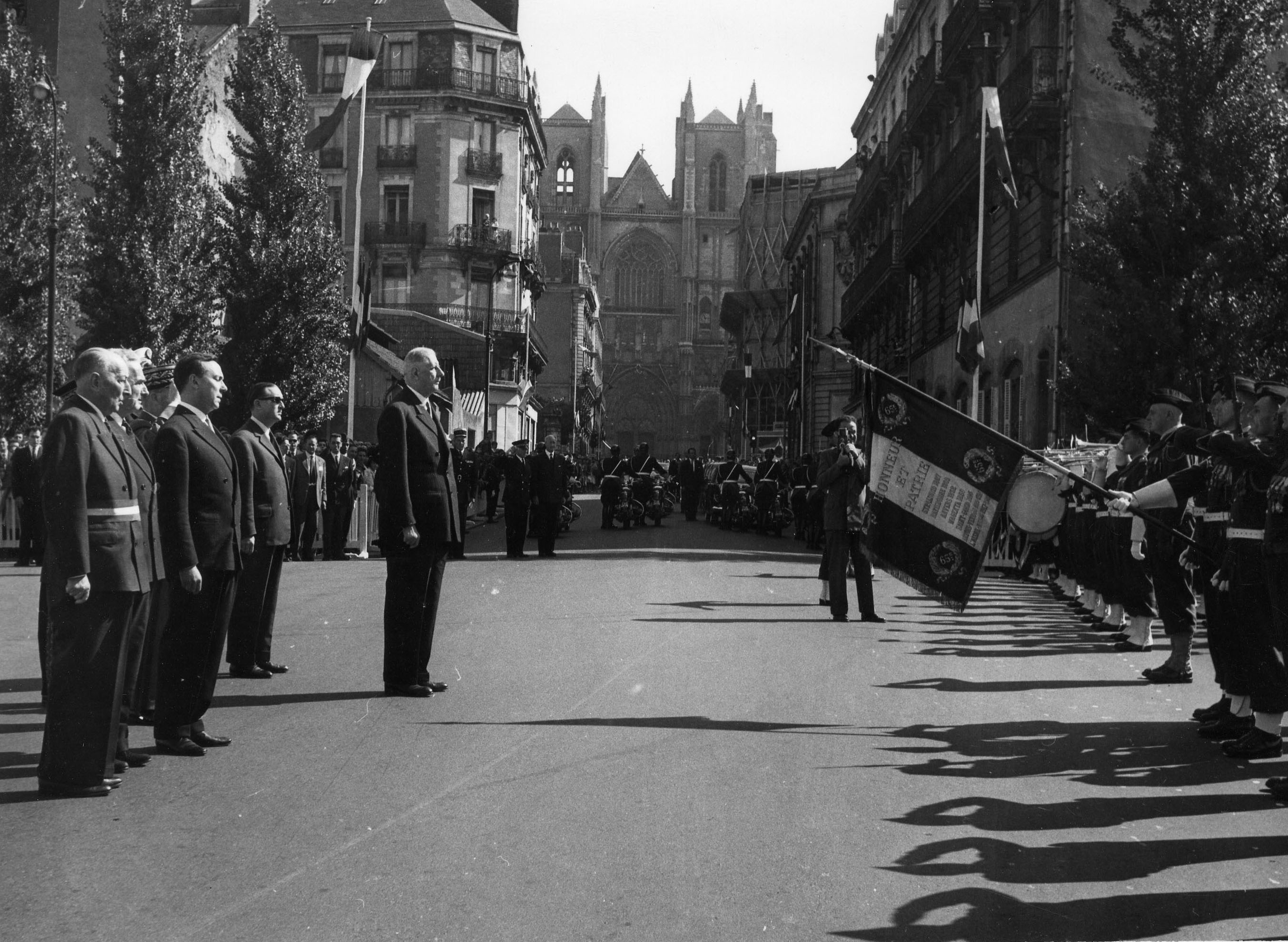 Le général de Gaulle, place de l'Hôtel de Ville, face au drapeau du 65e RI et à un détachement du 2e RIMA. Derrière lui, Henry Orrion, maire de Nantes, le général Massien, commandant la 3e Région militaire, et Michel Debré, Premier ministre, le 10 septembre 1960 (79Z5 - Fonds Régis Routier)
