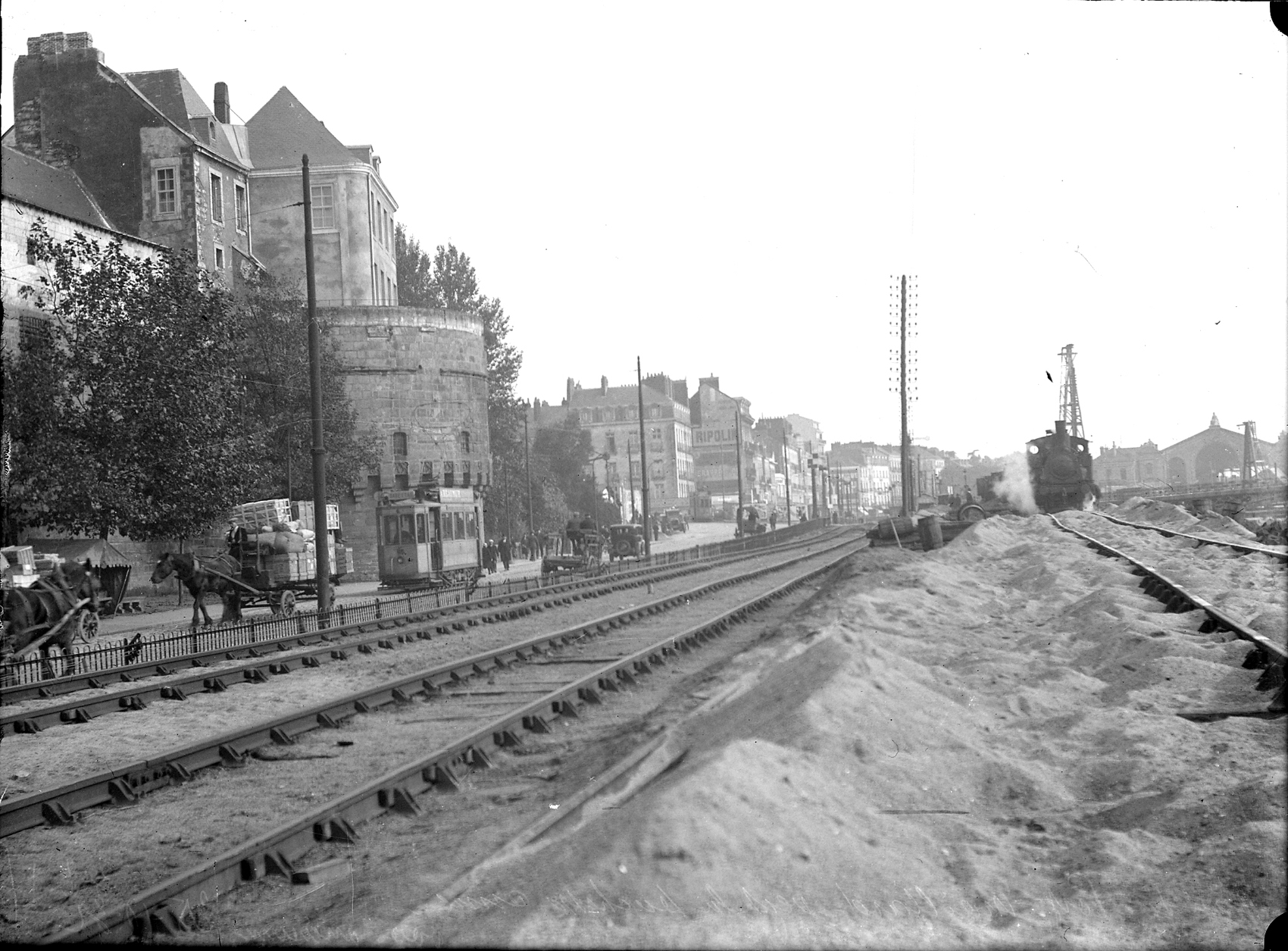 Sur cette photographie prise au début du 20e siècle, plusieurs types de véhicules se côtoient devant le château des ducs de Bretagne : une locomotive, un tramway, des automobiles et des charrettes à cheval (13Fi3585)