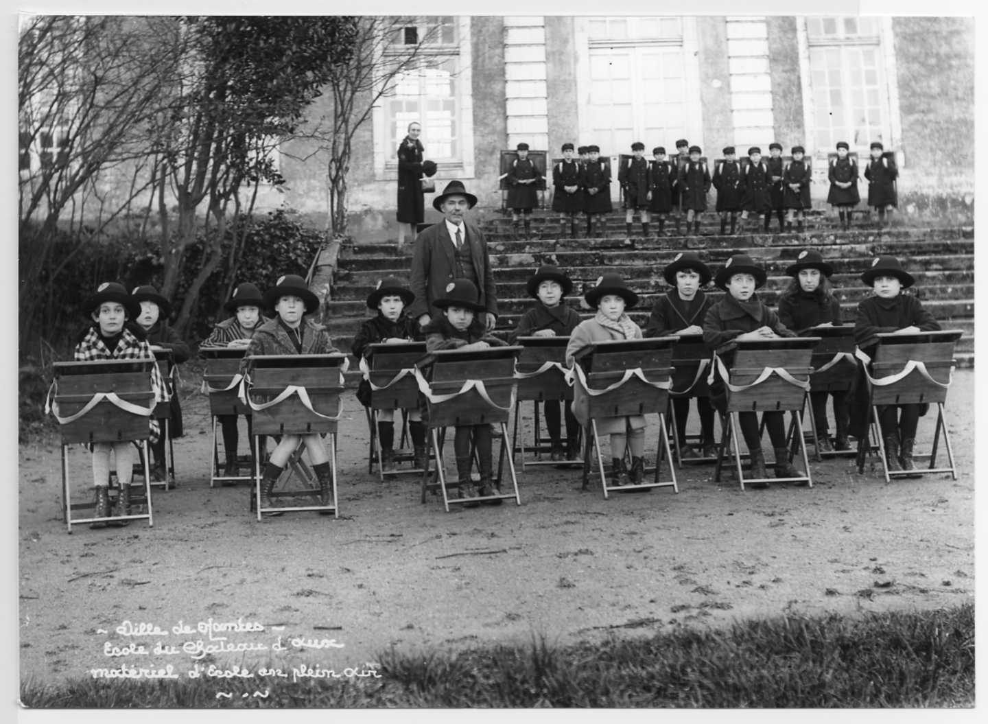 Des élèves de l'école de plein air du château d'Aux dans la cour du domaine, avec leurs tables de cours portatives, à la fin des années 1920 (13Fi935)