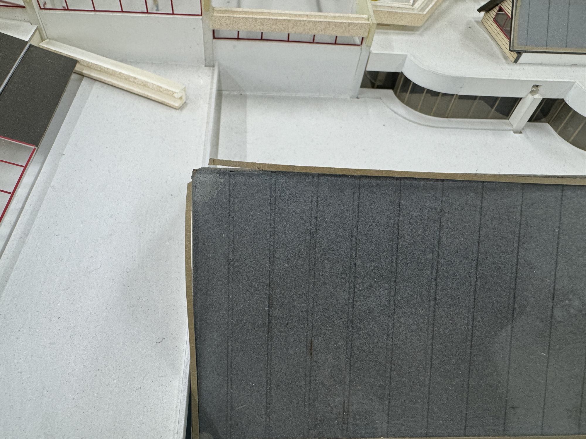 Détail de la maquette avant restauration : un élément en plexiglas désolidarisé et une perte d'adhésion d'un élément en papier sur le toit 