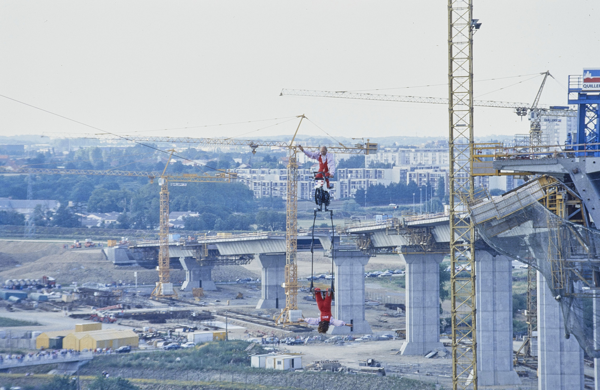 Le 13 juin 1990, les funambules Henry's et Jany's traversent la Loire à pied et à moto sur un câble tendu à la place du tablier du pont de Cheviré. Photographe : Régis Routier (17Fi6056)